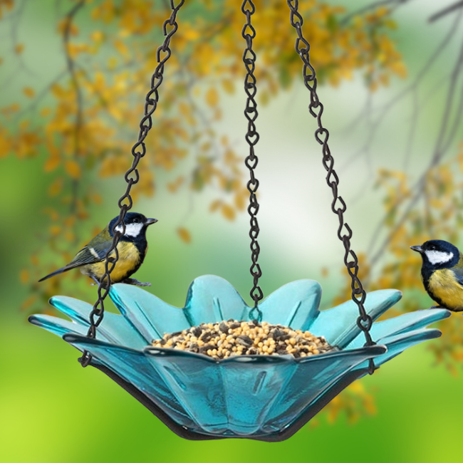 Two birds perched on the Flower Power Teal Glass Birdfeeder filled with birdseed